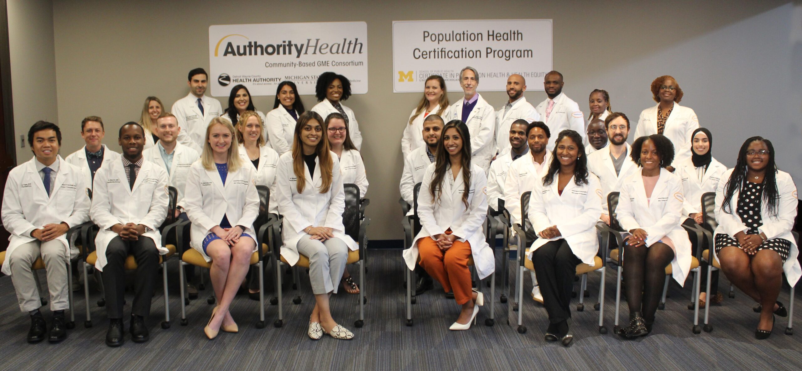Group of diverse health professionals posing in white coats at a certification ceremony.