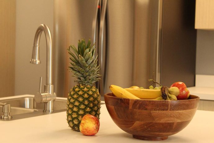 A pineapple, apple, and a wooden bowl of bananas on a kitchen counter.