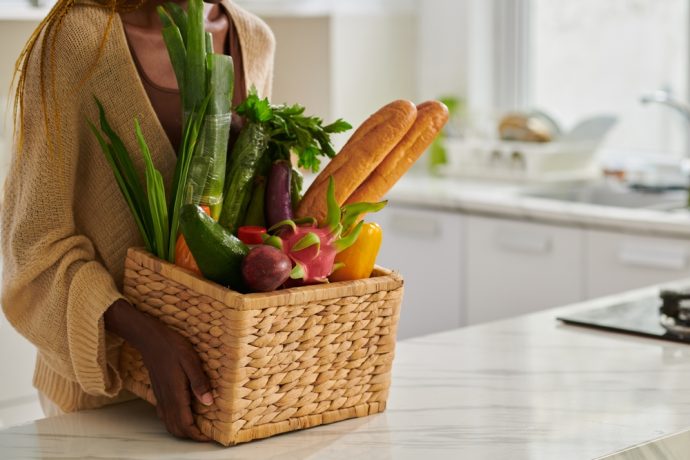A basket filled with fresh vegetables and baguettes in a kitchen.