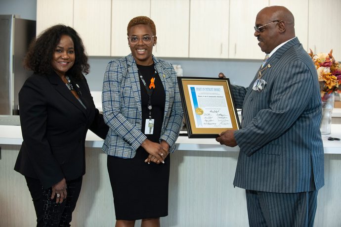 Three professionally dressed individuals exchanging a framed certificate or award.