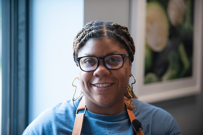 Smiling woman with glasses and braided hair in an apron.