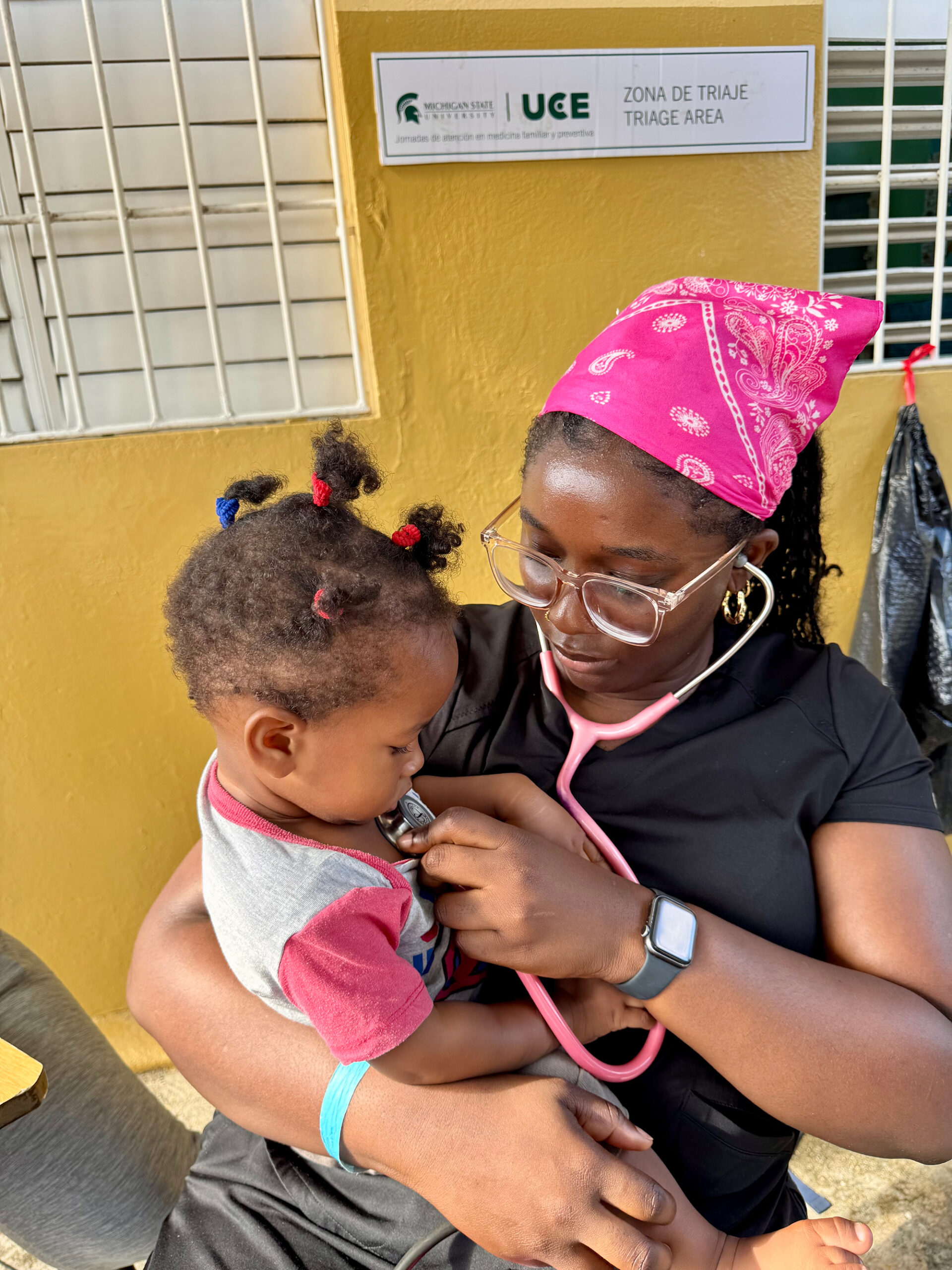 A woman in a pink headscarf holding a toddler in a warm moment.