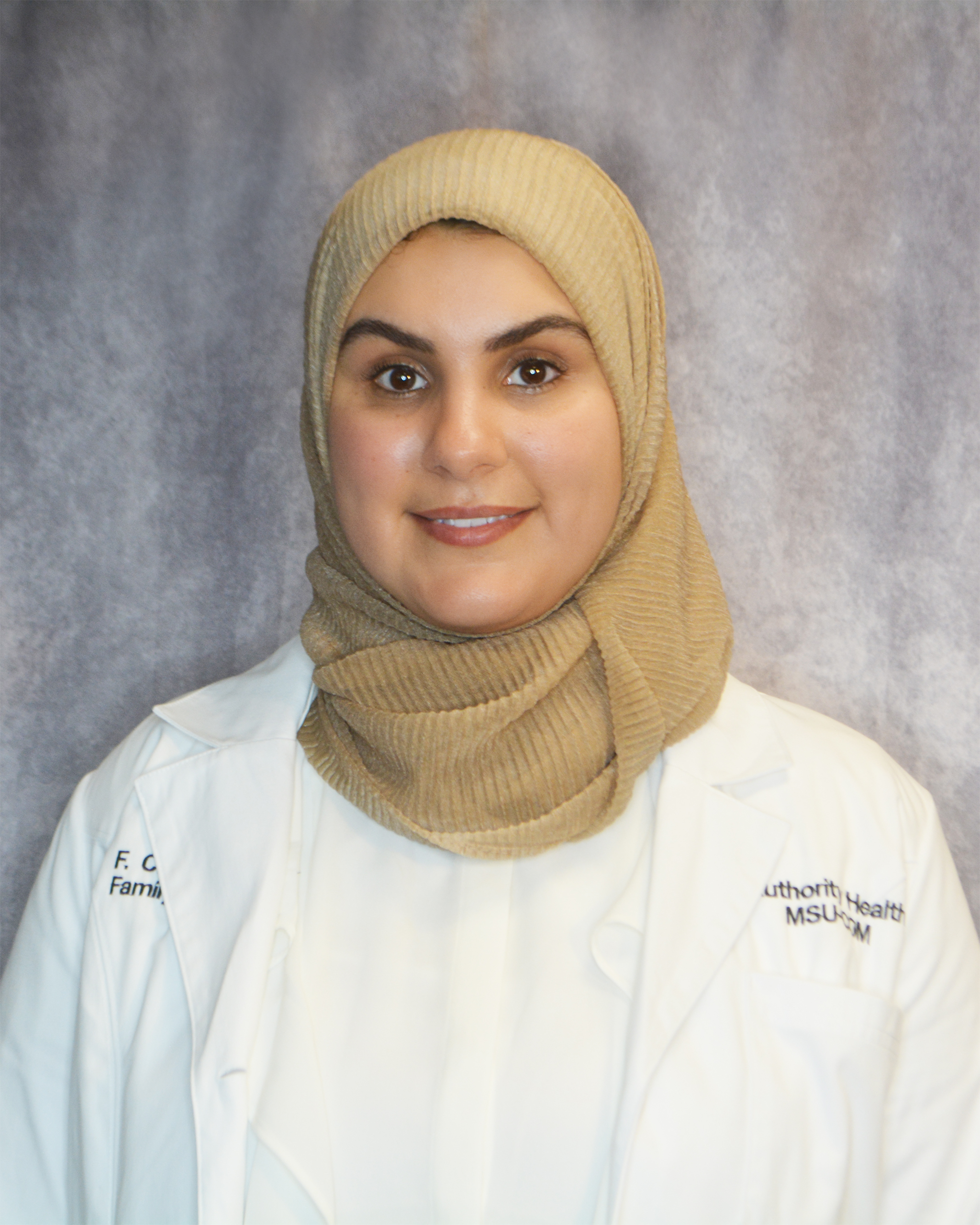 Professional woman wearing a beige hijab and white medical coat.