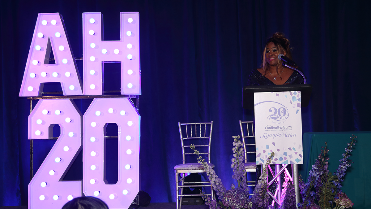 A speaker at a podium with large illuminated letters 'HO' on stage.