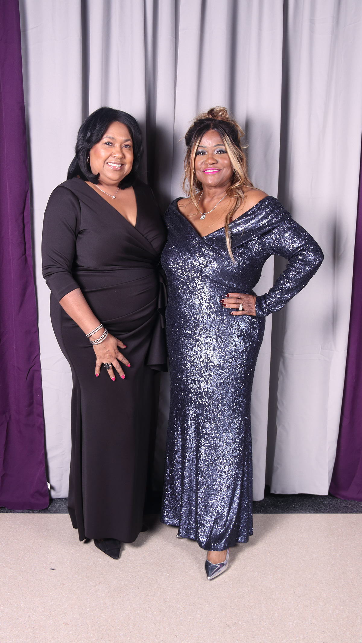 Two elegant women posing, one in black and one in a sparkling blue gown.