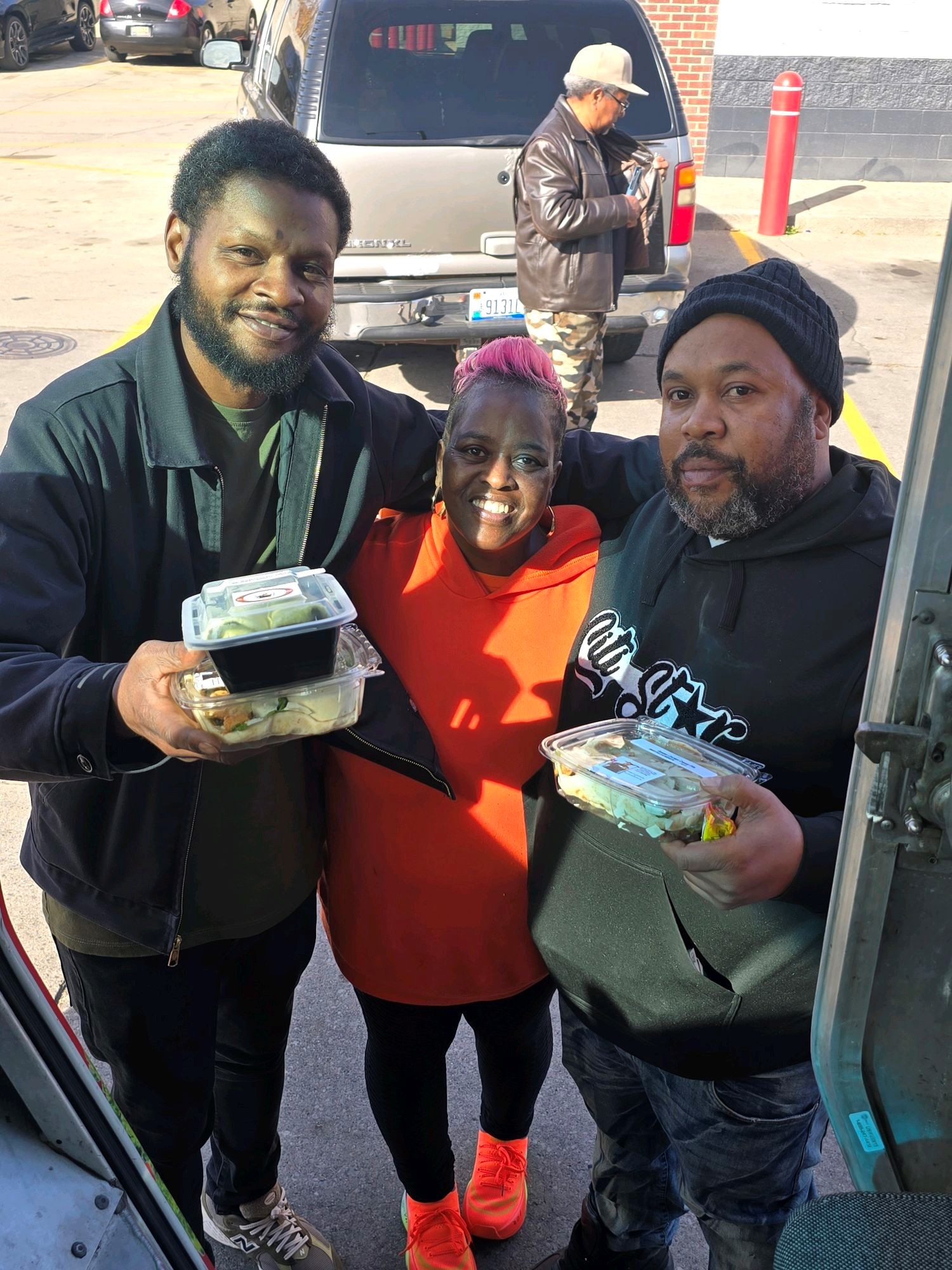 Three people smiling and holding takeout food containers.