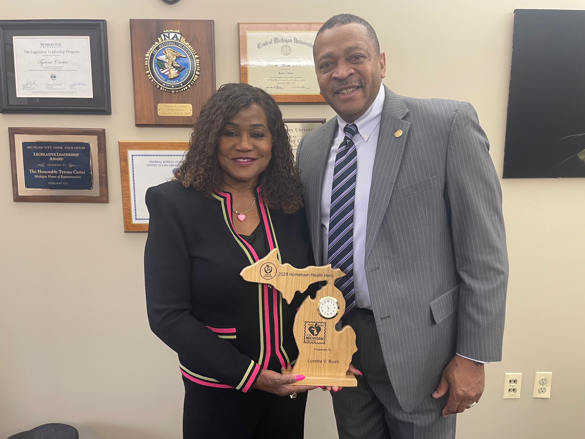 Two people smiling, holding an award plaque together indoors.