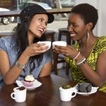 Two women clinking coffee cups at cafe