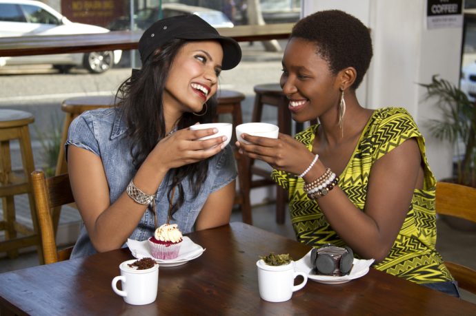 Two women clinking coffee cups at cafe